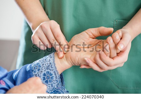 Cropped image of female caretaker checking pulse of senior woman at nursing home