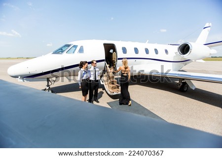 Elegant woman boarding private jet with airhostess and pilot at airport terminal