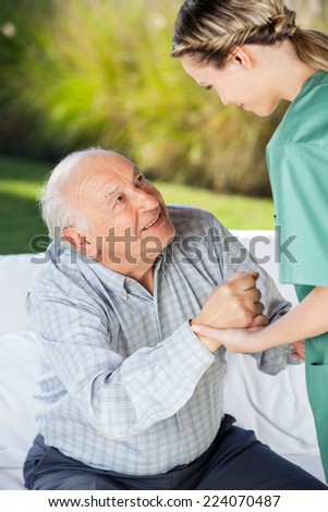 Female caretaker helping senior man to sit on couch at nursing home