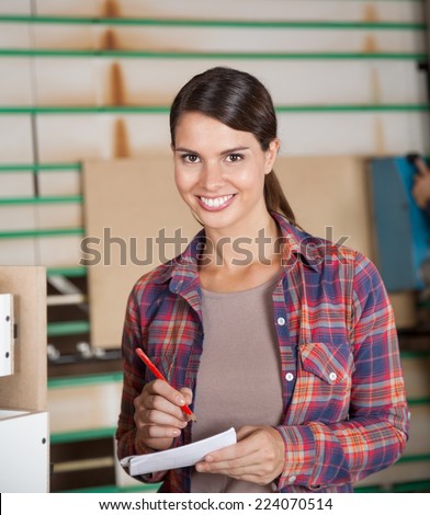 Portrait of confident female carpenter holding pencil and paper in workshop