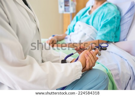 Midsection of female doctor sitting with patient on bed in hospital
