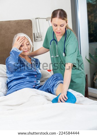 Female caretaker using hot water bottle on senior woman\'s leg at nursing home
