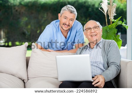 Portrait of happy male nurse and senior man with laptop on couch at nursing home porch