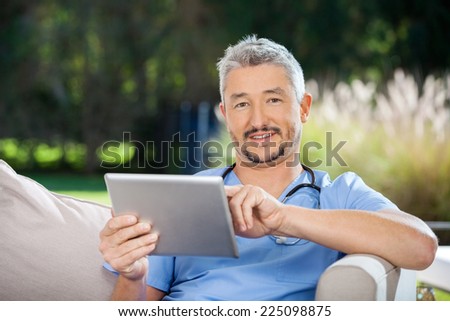 Portrait of male caretaker using tablet computer while sitting at nursing home porch