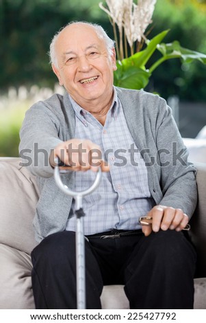 Portrait of happy senior man holding metal cane while sitting on couch in nursing home porch