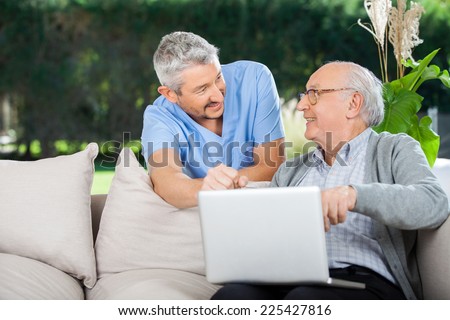 Smiling nurse and senior man looking at each other while using laptop at nursing home porch