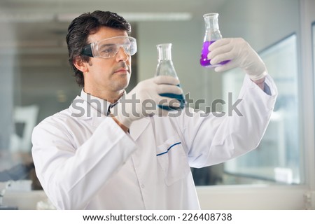 Male researcher examining flasks with different samples in lab
