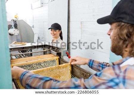 Portrait of happy young female beekeeper standing with colleague working in beekeeping factory