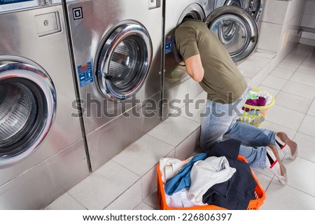 Young man searching clothes inside washing machine drum at laundromat