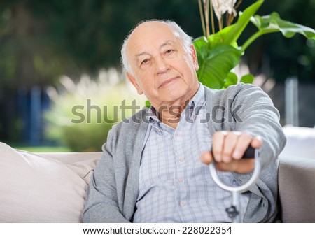 Portrait of senior man holding metal cane while sitting on couch in nursing home porch