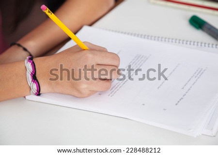 Cropped image of schoolgirl writing on paper at desk in classroom