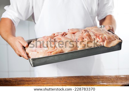 Midsection of mature butcher carrying tray filled with chicken pieces at counter in shop