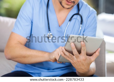 Midsection of male caretaker using tablet computer while sitting on couch at nursing home