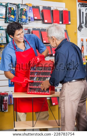 Smiling salesman showing tools to senior man in hardware store