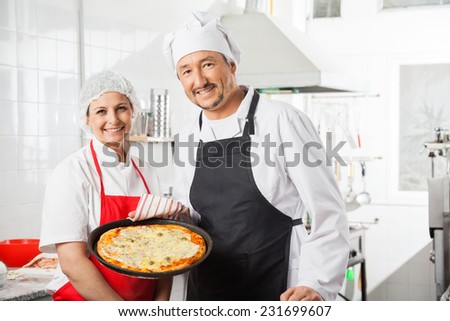 Portrait of confident male and female chefs with pizza pan at commercial kitchen