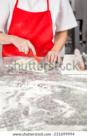 Midsection of female chef cutting ravioli pasta at messy counter in commercial kitchen