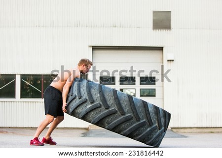 Full length side view of young male athlete flipping large tire outside gym