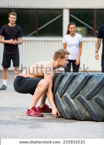 Side view of young male athlete flipping tractor tire outdoors
