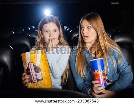 Woman looking at scared daughter watching movie in cinema theater