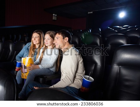Smiling family of three watching film in cinema theater