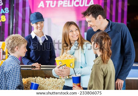 Happy family of four buying snacks from female seller at concession stand in cinema