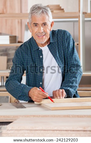Portrait happy senior male carpenter marking on wood with pencil in workshop