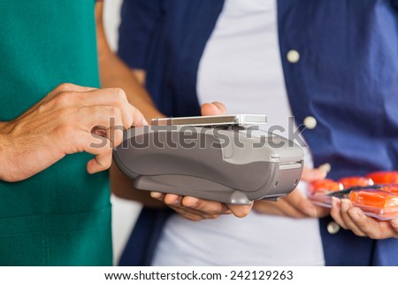 Worker accepting payment through smartphone with customer holding screwdriver set in store