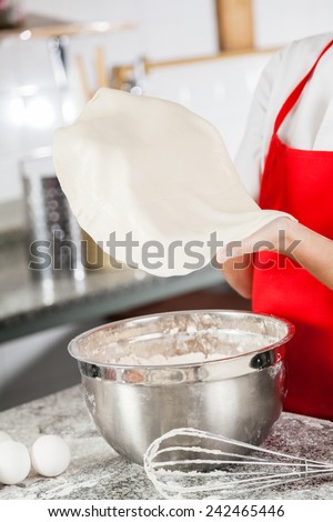 Midsection of female chef holding pasta sheet with mixing bowl and wire whisk on counter in commercial kitchen