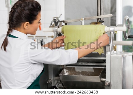 Rear view of female chef processing ravioli pasta in machinery at commercial kitchen