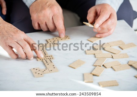 Copped image of senior couple playing dominoes at table in nursing home