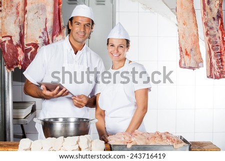 Portrait of confident male and female butchers with digital tablet at counter in shop