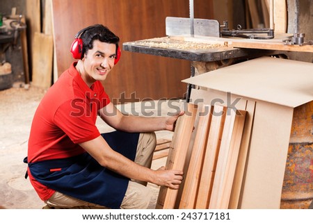 Portrait of confident young carpenter arranging wooden planks in workshop