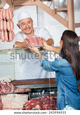 Mature man selling fresh packed of sausages to female customer in butchery