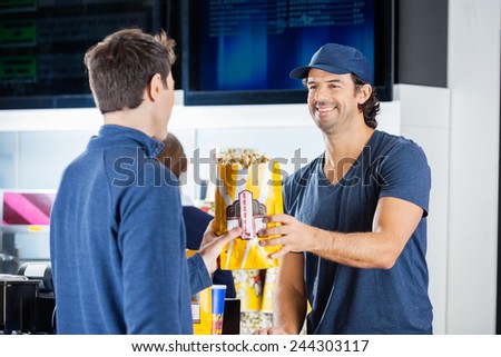 Smiling male seller giving popcorn paperbag to man at cinema concession stand