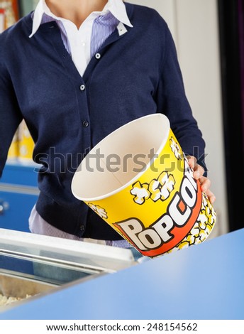 Midsection of female worker holding empty popcorn bucket at cinema concession stand