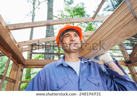 Smiling male worker carrying wooden planks at construction site