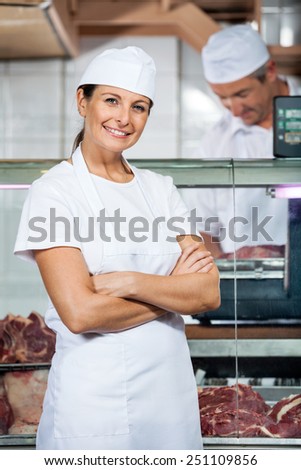 Portrait of confident female butcher with male colleague working in store