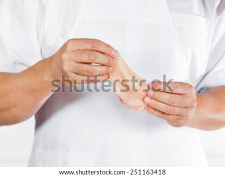 Midsection of mature butcher holding chicken meat in shop