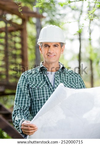 Portrait of smiling male architect holding blueprint at construction site