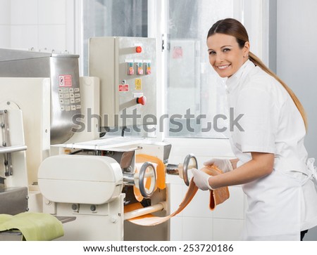 Side view portrait of female chef processing spaghetti pasta sheet in machine at commercial kitchen
