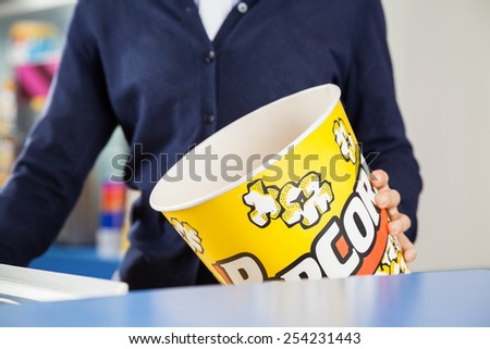 Midsection of female worker holding empty popcorn tub at cinema concession stand