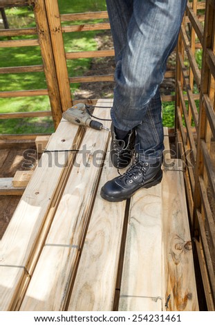 Low section of male construction worker standing by drill on stacked wooden planks at site