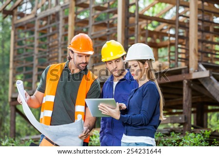 Male and female engineers using digital tablet while reviewing blueprint at construction site