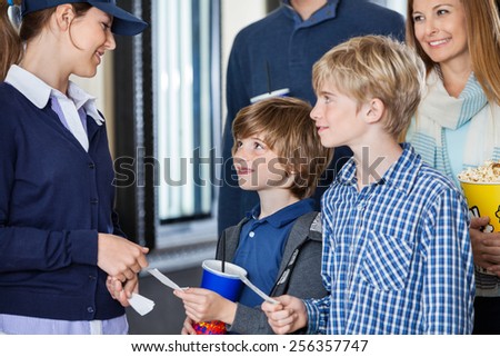 Boys giving movie tickets to female worker at cinema while parents standing in background