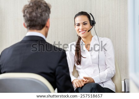 Happy female customer service representative wearing headphones talking to manager in office