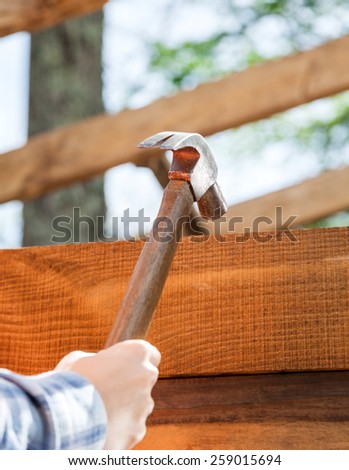 Female worker\'s hand hammering nail on timber frame at site