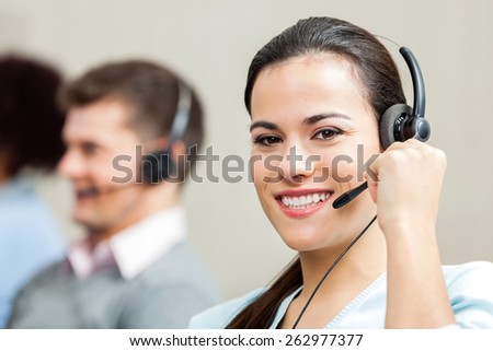 Portrait of confident female customer service executive with colleagues in background at call center