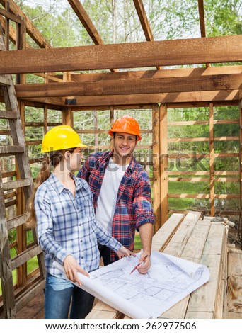 Portrait of happy male architect examining blueprint with female colleague in wooden cabin at site