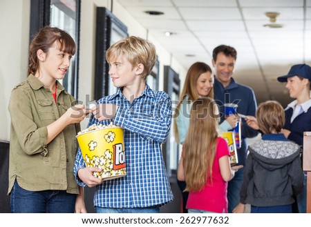 Brother giving movie tickets to sister at cinema with family and worker in background