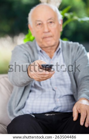 Portrait of elderly man using remote control while sitting on couch at nursing home porch
